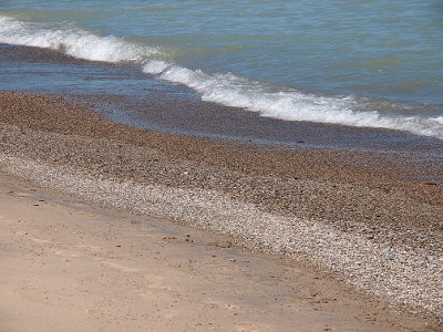 [Rows of stones the waves have washed to the shore. Sand on left, stone piles in middle, waves on right.]